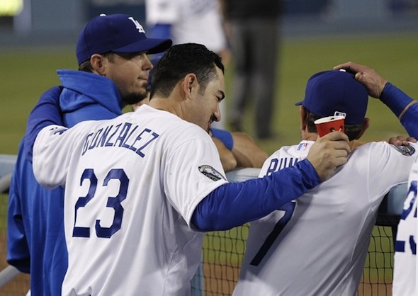 Los Angeles Dodgers first baseman Adrian Gonzalez (C) puts his arms around teammates pitcher Josh Beckett (L) and infielder Nick Punto (R) in the dugout during the fifth inning of an MLB baseball game against the Miami Marlins in Los Angeles August 25, 2012. Gonzalez, Beckett, and Punto were all acquired from the Boston Red Sox along with pitcher Carl Crawford in a nine player trade.