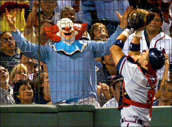 A fan dressed as a clown tries to distract Atlanta Braves catcher Javy Lopez (R) as Lopez catches a pop foul off the bat of the Boston Red Sox Dante Bichette in the seventh inning at Fenway Park in Boston, Massachusetts July 6, 2001.