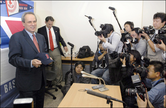 Red Sox President Larry Lucchino, left, holding the major league team's baseball cap is surrounded by Japanese photographers during a news conference in Tokyo Tuesday, Nov. 28, 2006, after meeting with representatives of Daisuke Matsuzaka's team, the Seibu Lions.