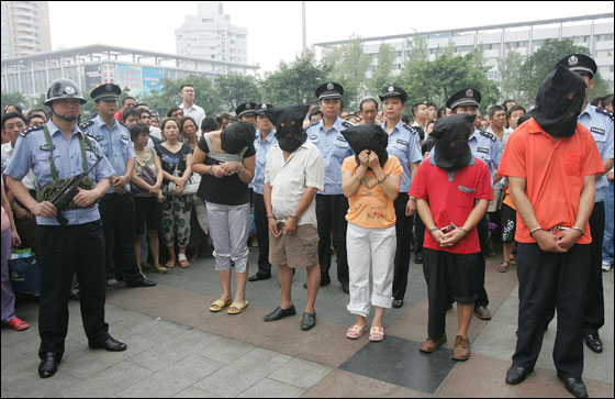 Armed policemen guard people accused of swindling, stealing and ticket scalping during a public sentencing rally at the Railway North Station in Chengdu in China's southwest Sichuan province Wednesday, Aug. 16, 2006. Thirty criminals were sentenced during the campaign.   Local authorities have launched campaigns to crack down on ticket scalping, swindling and stealing in order to assure the safety of passengers and improve the order of railway stations.