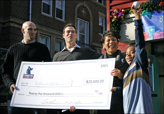Paul Epstein, left, his brother Theo, middle left, and Joan Wallace-Benjamin, President and CEO of The Home for Little Wanderers, middle right, all react to Nicholas Davis, of Brockton, Mass., while he holds a baseball given to him from Theo high in the air during a press conference to kick off a gift drive for The Home for Little Wanderers in Boston on Thursday.